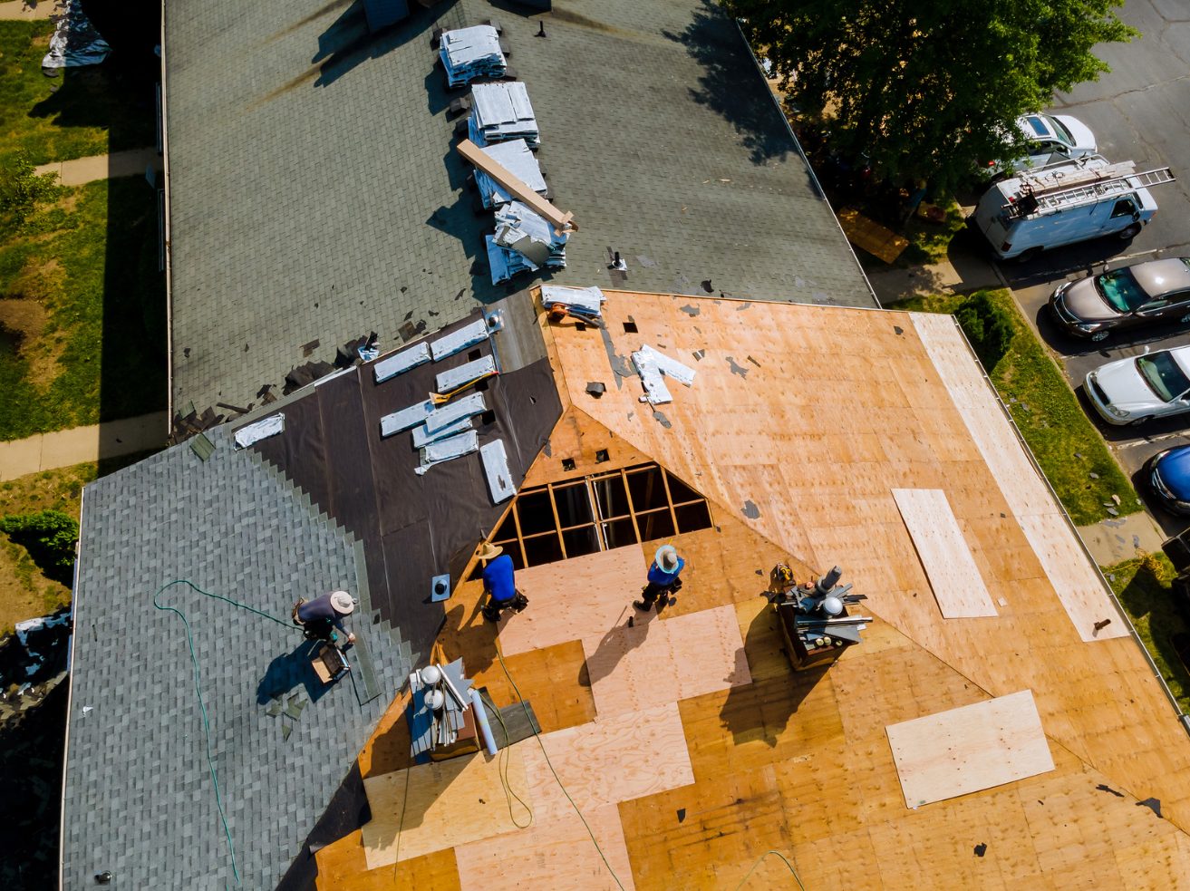 Overhead aerial view of a roof partway through replacement, with old shingles, bare sheathing, and crew at work